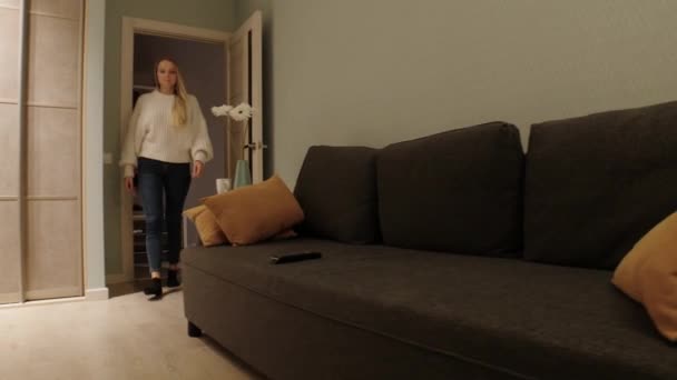 Uma mulher caminha em uma sala de estar e liga a TV — Vídeo de Stock