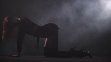 Karanlık dumanlı stüdyoda yerde dans eden uzun bacaklı çekici bir kadın.