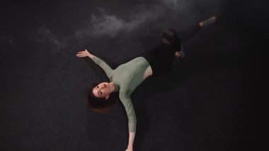 Esmer dumanlı stüdyoda seksi ince kadın yerde dans ediyor.