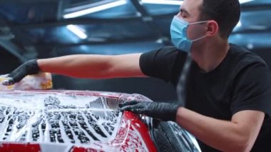 Oto yıkama - adam temizlik köpüğü ve süngerle kırmızı bir arabayı yıkıyor.