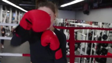 Genç ve çekici bir kadın boks antrenmanını spor salonunda kameraya karşı yapıyor.
