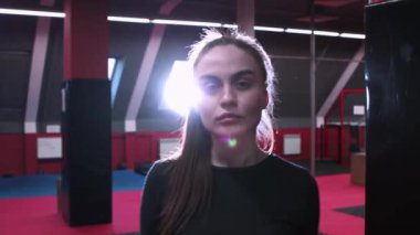 Çekici genç bir kadın yumruklarını kırmızı spor salonundaki kum torbasında eğitiyor.