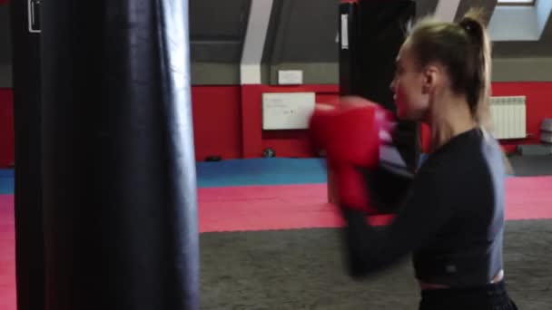 Молодая женщина тренирует свои удары в боксерскую грушу — стоковое видео