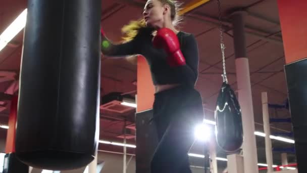 Молодая женщина тренирует свои удары в боксерской груше в спортзале — стоковое видео