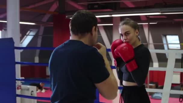 Тренажерный зал - молодая женщина тренирует свой бокс на ринге с тренером - тренирует оборонительную технику — стоковое видео