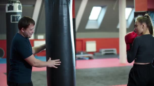 Boksen training - een aantrekkelijke vrouw ponsen de tas en haar coach staan achter het — Stockvideo