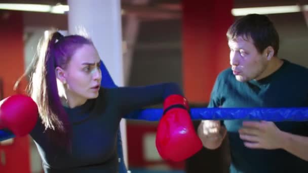 Uma jovem atraente descansando no ringue de boxe e seu treinador fala com ela — Vídeo de Stock