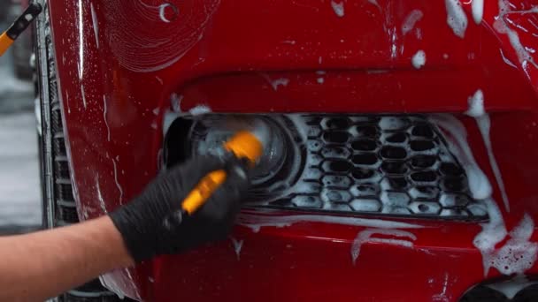 Serwis automatycznego czyszczenia - człowiek nakładający piankę czyszczącą na czerwony samochód — Wideo stockowe