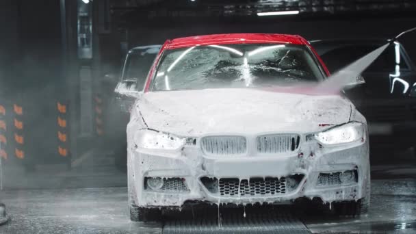 Авто детализация - работник заливает воду над автомобилем, смывая слой пены — стоковое видео