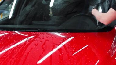 Araba yıkama servisi. Adam araba yüzeyindeki suyu bez parçasıyla siliyor.