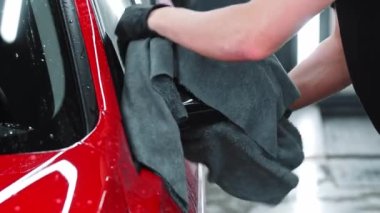 Araba yıkama servisi. Adam kırmızı bir arabanın suyunu bez parçasıyla siliyor.
