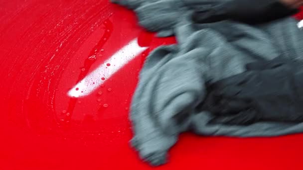 Usługa mycia samochodów - człowiek wyciera wodę z czerwonej powierzchni samochodu szmatą — Wideo stockowe