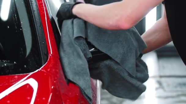 Servicio de lavado de coches - el hombre limpia el agua de un coche rojo con trapo — Vídeos de Stock