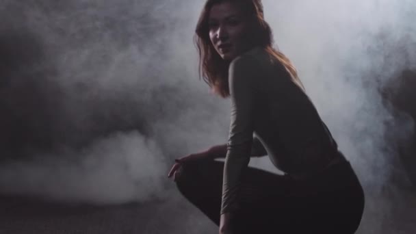 Young sexy woman dances in the dark smoky room - stands up from the floor — Stock Video