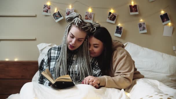 Novias acostadas en la cama y leyendo libros y tomadas de la mano — Vídeo de stock