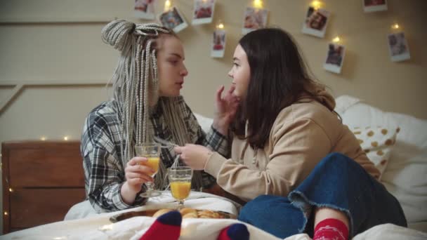 Jóvenes lesbianas desayunando en la cama - bebiendo jugo y jugando con el pelo — Vídeo de stock