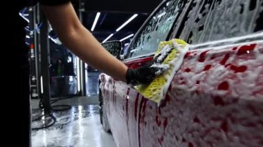 Bir adam arabanın yanında köpükle kaplı bir sünger tutuyor.