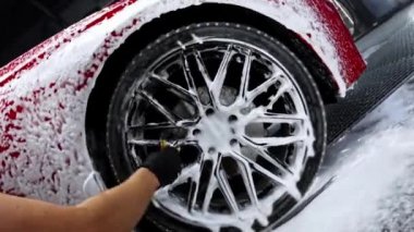 Bir adam arabanın direksiyonundaki diskleri köpük ve fırçayla temizliyor.
