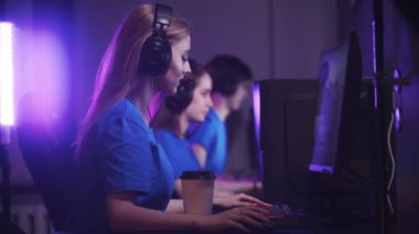 Bir grup arkadaş oyun kulübünde oturup online oyun turnuvası yapıyorlar. Ön planda kahve içen bir kadın.