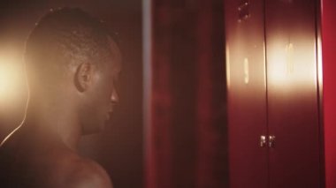 Siyah bir adam soyunma odasındaki bir anahtarla dolabını açıyor.