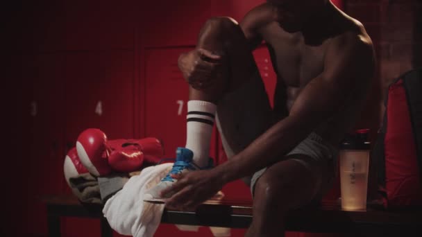 Svart ung man boxare binda upp sina sneakers i ett omklädningsrum — Stockvideo