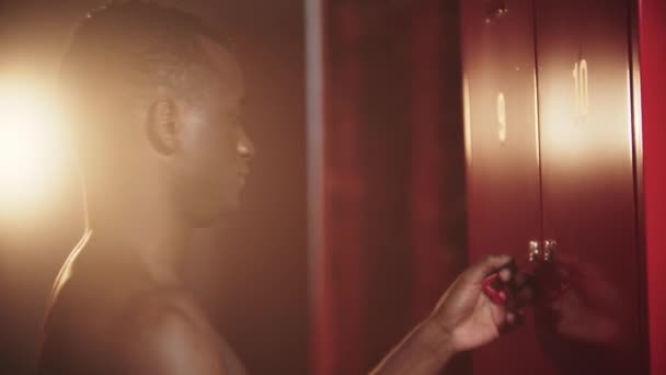 Een zwarte man die zijn kluisje opent op een sleutel in de kleedkamer en de bokshandschoenen uitdoet. — Stockvideo