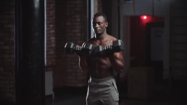 Um homem negro bombeando as mãos músculos com halteres no ginásio — Vídeo de Stock
