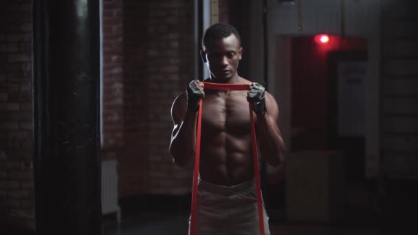 Un bell'uomo nero che pompa i muscoli delle mani in palestra tirando la cintura attaccata ai pesi — Video Stock