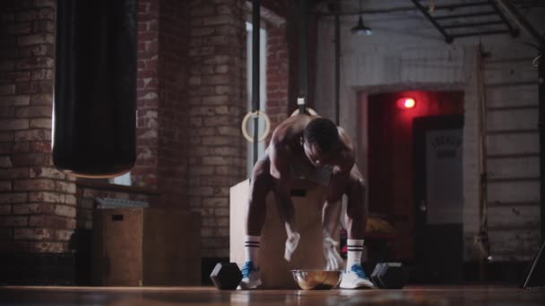 Un bel homme noir s'entraîne dans la salle de gym - couvrant les mains de craie et soulevant des haltères — Video