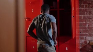 Afro-Amerikan atletik genç adam soyunma odasında üstünü değiştiriyor.