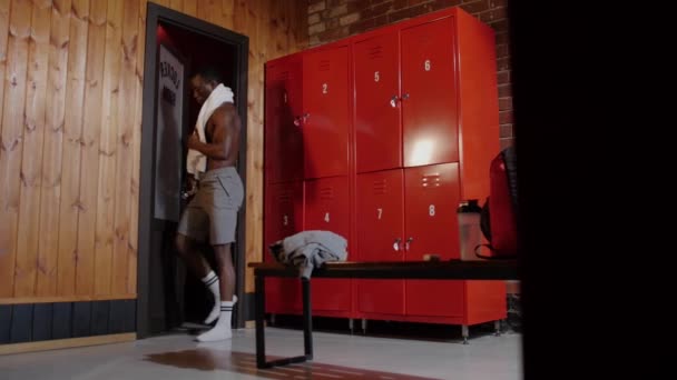 Afro-Amerikaanse atletische jongeman loopt in de kleedkamer na de douche en gaat zitten op de bank — Stockvideo