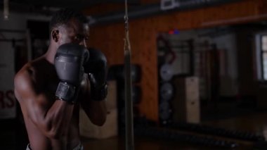 Afro-Amerikan atletik yarı çıplak genç adam boksör eğitimi. Spor salonundaki kum torbasında.