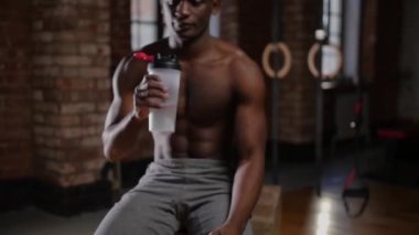 Spor salonunda plastik şişeden su içen, üstsüz, Afro-Amerikalı yakışıklı bir adam.