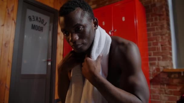 Jovem atlético afro-americano semi-nu sentado no vestiário e limpando a cabeça com uma toalha — Vídeo de Stock