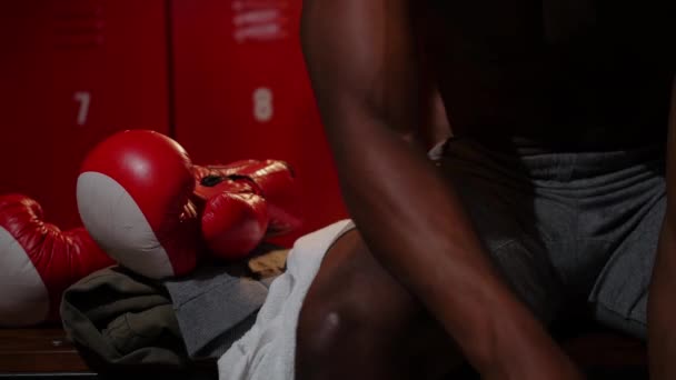Afro-americano atlético meia nua jovem boxeador sentado no banco no vestiário e se preparando para o treinamento — Vídeo de Stock