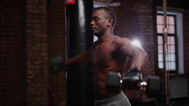 Een Afrikaans-Amerikaanse man pompt zijn handen spieren met halters in de sportschool — Stockvideo