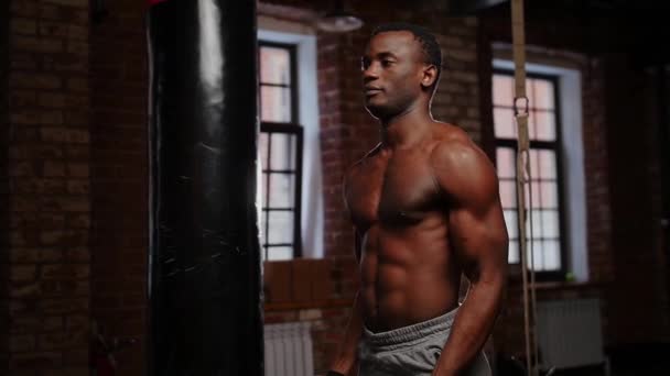 Un joven afroamericano guapo bombeando los músculos de sus manos con dos pesas en el gimnasio — Vídeos de Stock