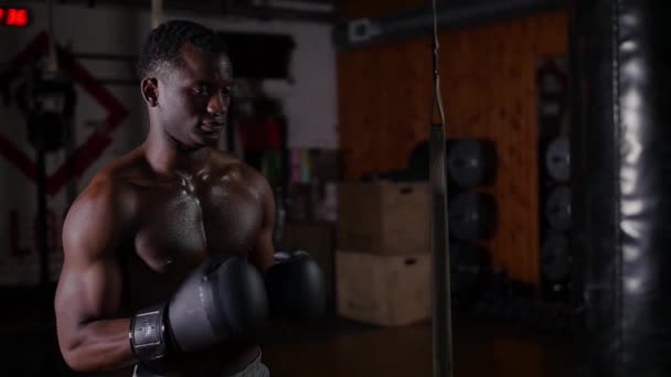 Афроамериканець, напівголий молодий боксер, дивиться на торбу в спортзалі. — стокове відео