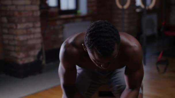 En skjorteløs, afroamerikansk kjekk mann som trener i gymmen, drikker vann og ser inn i kameraet – stockvideo