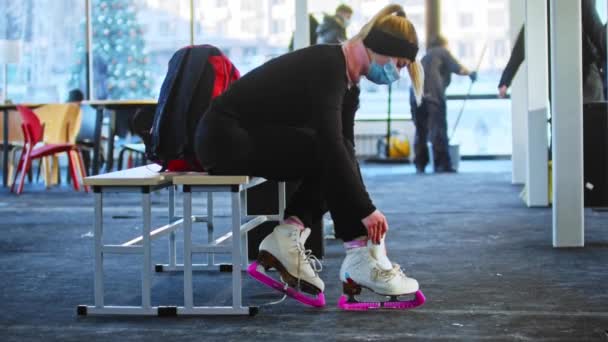 Vrouw met masker dassen schoenveters op witte schaatsen in kleedkamer — Stockvideo