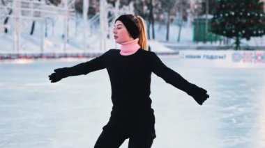 Artistik buz pateni pistinde antrenman yapan ve kameraya bakan genç bir kadın.