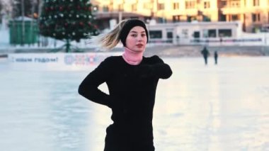 Genç, güzel bir kadın buz pateni pistinde artistik patinaj eğitimi alıyor ve kameraya bakıyor.