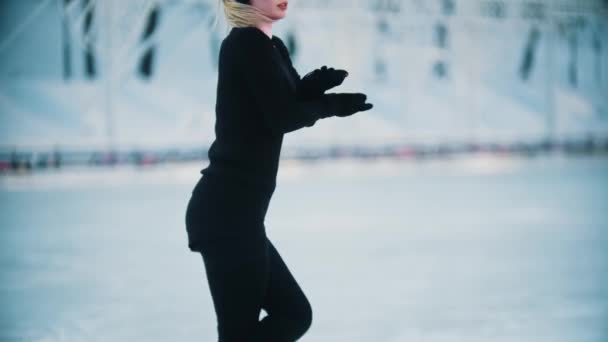 Fiatal nő fekete ruhában magas lófarok figura korcsolyázás a nyilvános jégpályán — Stock videók