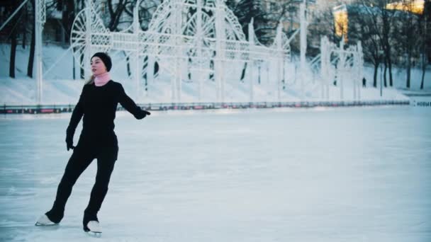 Jonge blonde vrouw in zwarte kleren met hoge paardenstaart figuur schaatsen op de openbare ijsbaan — Stockvideo