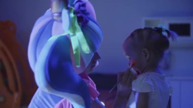 Animatör, kızların yanaklarına makyaj yaparak turuncu neon bir kalp çizer.