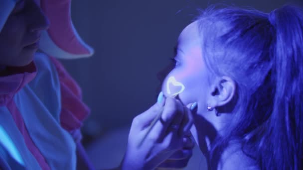 Animador desenha uma maquiagem de néon na bochecha das meninas — Vídeo de Stock
