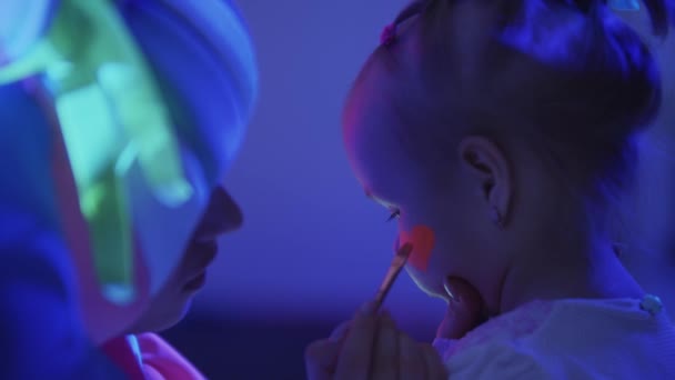 Animator tekent een oranje neon hart met make-up op meisjes wang - circus show — Stockvideo