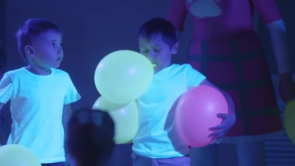 Kinderen en animators spelen met ballonnen in de neonkamer tijdens de show — Stockvideo