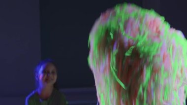 İki küçük gülümseyen kız arkadaş renkli kurdeleler fırlatırken neon şov