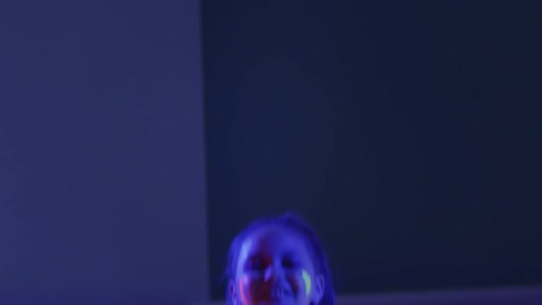 En liten leende flicka spyr upp färgglada band medan neon visar — Stockvideo